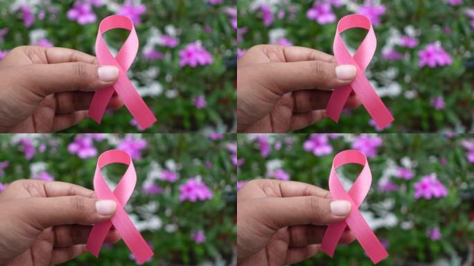 粉色丝带乳腺癌意识图标徽章在花和绿叶背景上的手指上举行。世界癌症日，10月粉红日，全国癌症幸存者日概