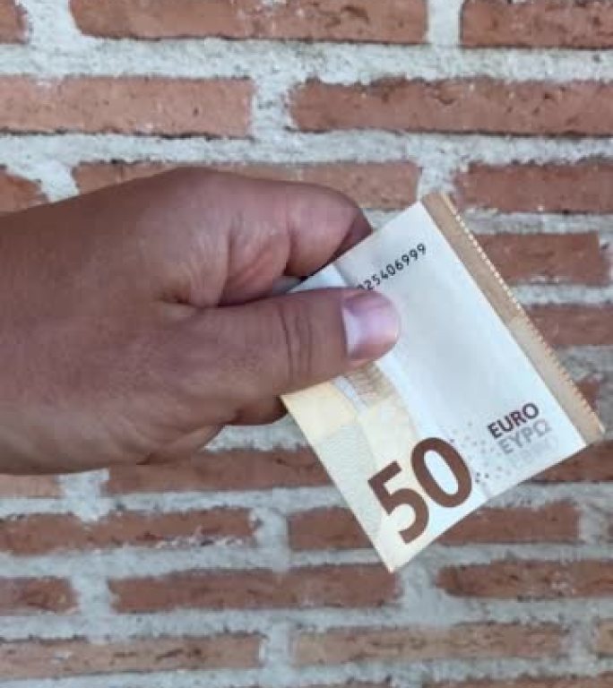 无法识别的人的手将折叠的50张钞票交给另一个人，后者捡起并走开了。背景为砖墙的金钱掉落的特写视频。经