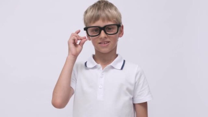 白色背景上戴着眼镜的肖像男生。回到学校。有趣的男孩竖起大拇指微笑。学生欢笑而欢喜。快乐积极的孩子。快