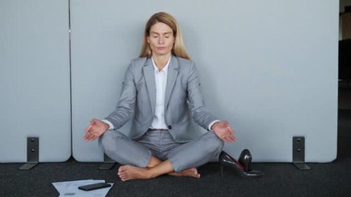 荷花姿势紧张的女员工坐在地板上，没有鞋子闭着眼睛冥想工作中休息，保持精神平衡耐心瑜伽练习没有压力感觉