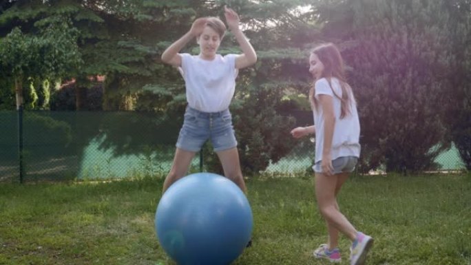 三胞胎姐妹女孩青少年在后院草地上与健身蓝球一起玩耍，踢它，推它，扔它，跳跃和滚动