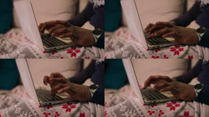 在笔记本电脑键盘上打字的非洲人的手的特写。那家伙按手指在钥匙上。他手头有手表。膝盖被毯子遮住了