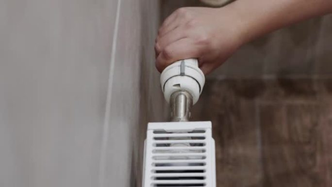 一名男子调节散热器上的恒温器，以更好地加热房间。采暖季，水暖价。特写