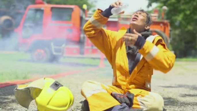 消防员坐在消防车或消防车前，用水倒在他的脸和嘴上，看起来他完成并成功区分火