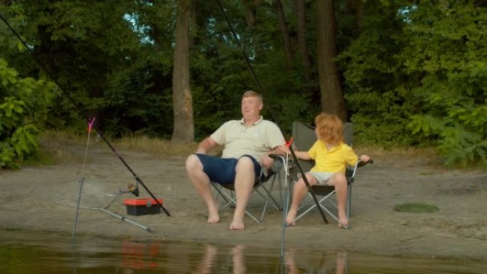可爱的学龄儿子和父亲用旋转钓鱼竿在池塘上抓鱼