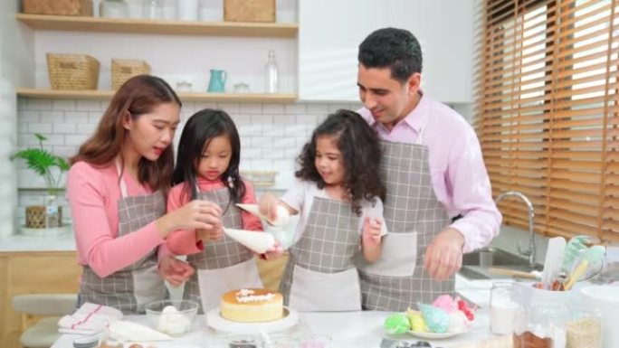 年轻的小女孩站在家里现代厨房的柜台烘焙面包店。快乐微笑的父母喜欢周末。孩子和母亲穿着围裙在自制蛋糕上