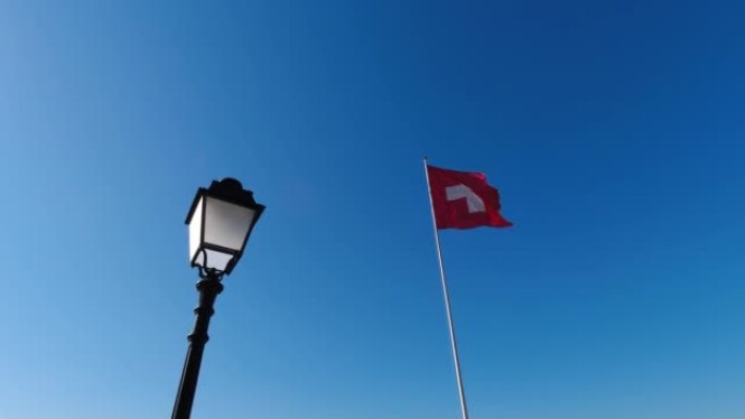 瑞士国旗，前面是旧灯。瑞士国旗在风中挥舞，背景中仿古油灯在风中挥舞