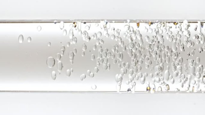 透明化妆品凝胶流体，分子气泡和油在玻璃管中流动，白色背景上有透明液体。宏观拍摄。生产特写。慢动作。