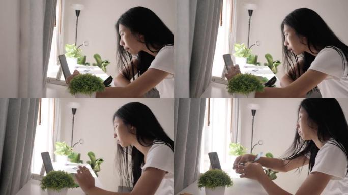亚洲少女吃一些零食，通过智能手机在家窗口附近观看病毒视频或电影，生活方式概念。