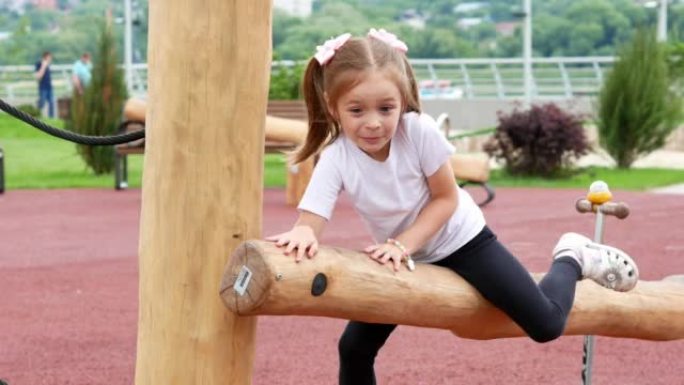 一个有两条尾巴的快乐小女孩坐在一根大木头上，快乐地在一个有障碍的现代运动场上玩耍