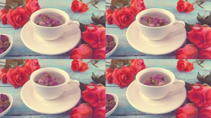 白色的茶帽，带有芬芳的干玫瑰花蕾，新鲜的玫瑰花放在老式的浅蓝色木制桌面上。茶冲泡。