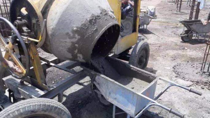 混凝土搅拌机将湿水泥倒入独轮车中。柴油混凝土搅拌机将湿水泥倒入独轮车的特写视频