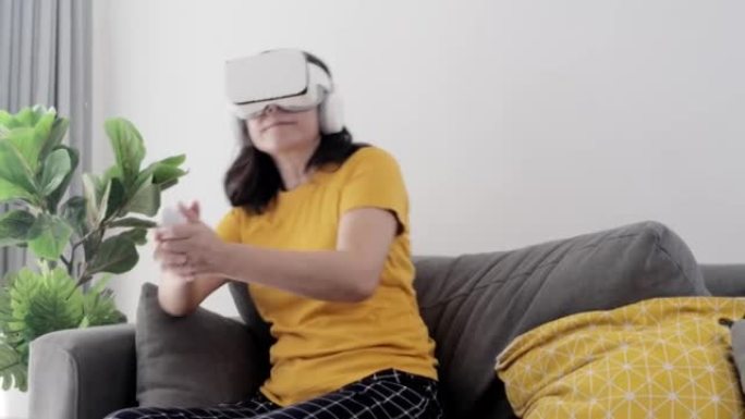 亚洲成年母亲试图通过虚拟现实在家里窗户附近的沙发上玩游戏，科技生活理念。