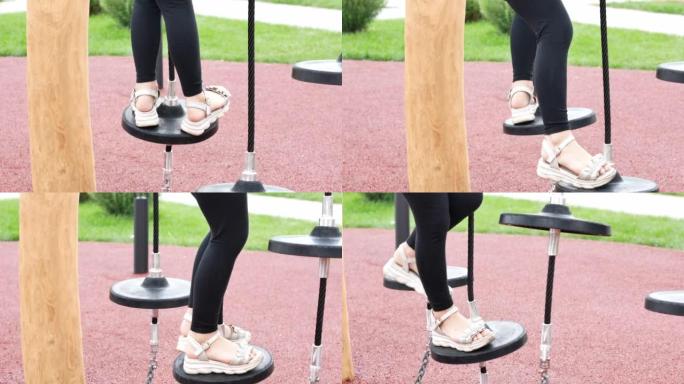 夏季凉鞋中儿童脚的特写镜头克服了绳索公园上的障碍，孩子正在平衡寻找平衡。现代儿童木制游乐场