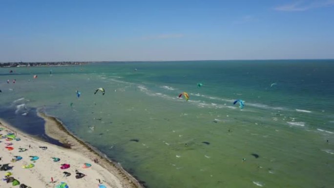 许多风筝冲浪者的天线，五颜六色的风筝飞过蓝色的泻湖，骑在风筝板上。在大风天，风筝冲浪者用降落伞在海浪