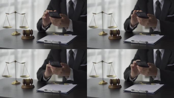 一位亚洲男性律师正在使用智能手机向办公室的客户咨询，法庭桌子上的木锤和带有笔记本电脑正义和法律概念的