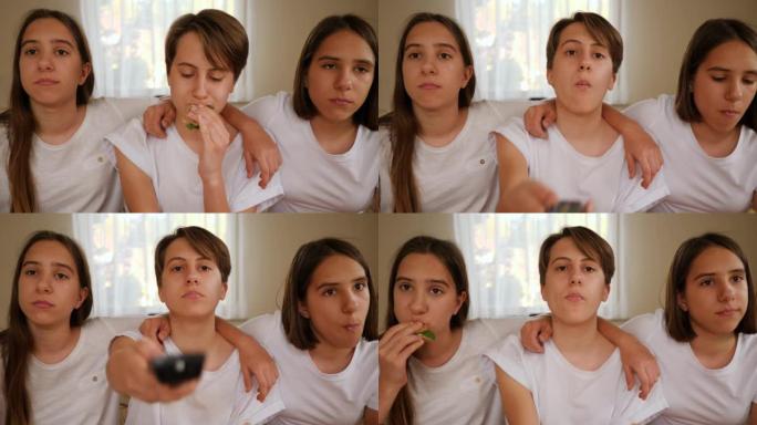 三胞胎姐妹十几岁的女孩在家看电视，坐在沙发上一起吃美味的三明治