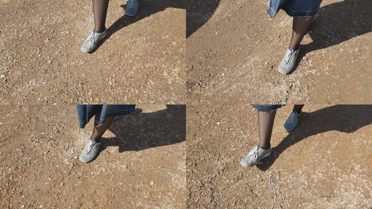 穿着运动鞋和黑色紧身衣的女人的脚在公园的碎石路上