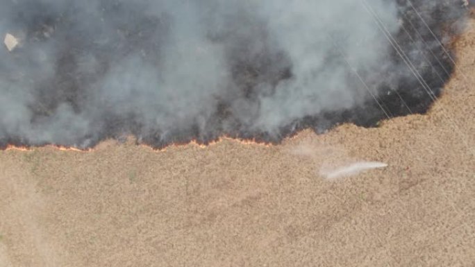 田地里的庄稼着火了。从直升机上鸟瞰。在棕灰色的烟雾中飞行。巨大的红色火焰和正在工作的消防员和消防车。