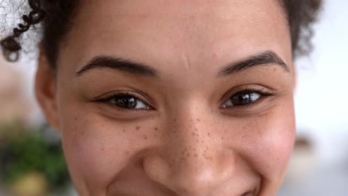 一个非洲裔美国千禧一代卷发女孩微笑着看着镜头的特写镜头。一个皮肤黝黑的积极的雀斑女孩的眼睛
