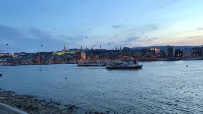 多瑙河在傍晚一艘船在远处的桥上飞着许多乌鸦和鸽子，在傍晚非常美丽，一切都在蓝色03.04.22匈牙利