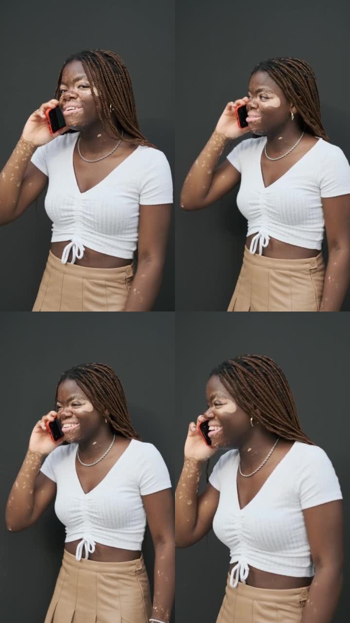 患有白癜风的非裔美国妇女在电话上微笑着站在黑色的墙壁上。