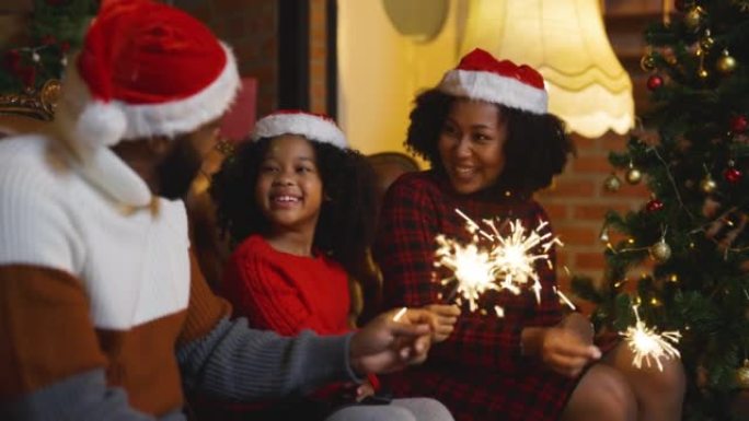 与父亲，母亲和女儿一起关闭非裔美国人家庭，晚上在圣诞树附近与play spakler一起享受圣诞节，