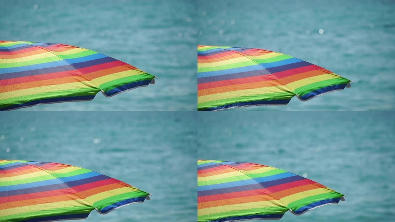 在海滩上阳光明媚的日子里，彩虹色的沙滩伞或遮阳伞抵御蓝色的大海。假期、放松、夏天的象征。阳光下的五颜