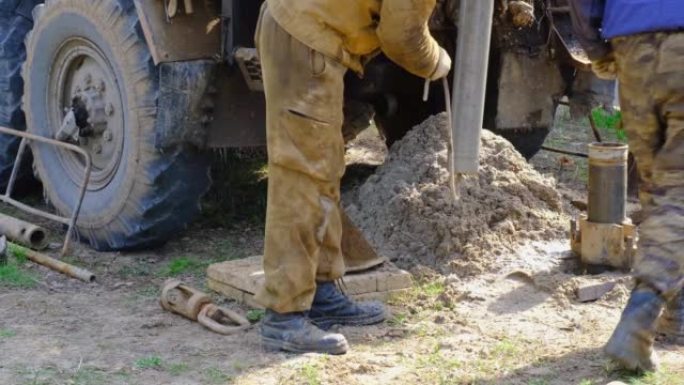 在汽车上安装钻机的工人团队正在钻探自流井以获取地下水。将金属套管插入地面，安装个人饮用水