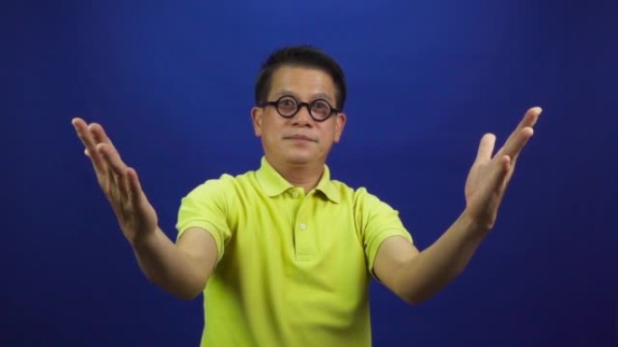 穿着休闲的黄色t恤的聪明的中年亚洲男人的肖像在工作室中呈现蓝色背景上孤立的东西，看起来很有魅力