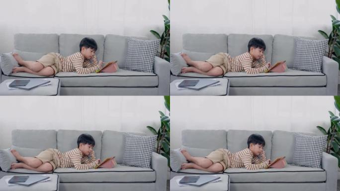 4K，慢动作，英俊的亚洲男孩，躺在沙发上舒适的位置，双手放在脚上，下巴，他在平板电脑上玩游戏，在学校