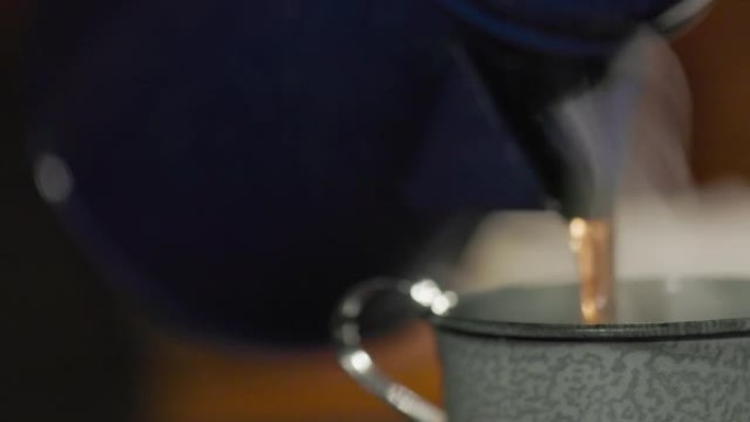 将新鲜酿造的热气腾腾的牛仔风格咖啡从老式水壶倒入锡杯中。