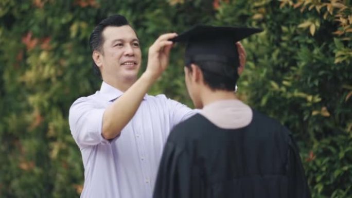 骄傲的亚洲马来父亲为他的儿子在大学大楼外的大学毕业礼服上调整了迫击炮，为毕业典礼做准备