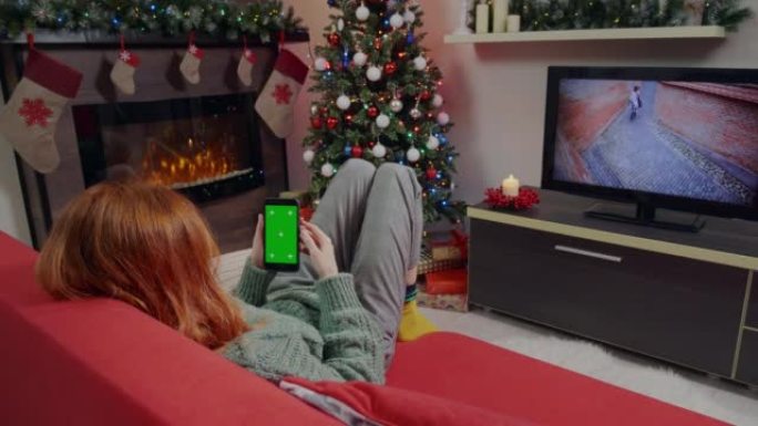 一个红头发的女人在装饰好的客厅里点击并滚动绿屏手机。
