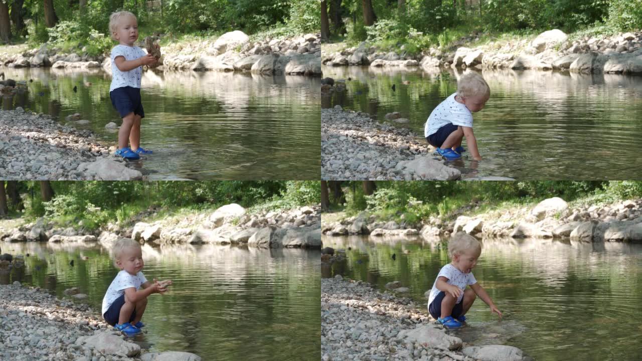 1.5岁的小孩在夏季公园的河岸上玩耍，喜欢将鹅卵石扔进水中。