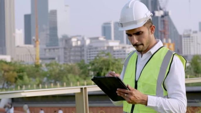 印度工程师的工人介绍了带有智能平板电脑的项目，以检查和站立在具有城市和建筑背景的室外空间。