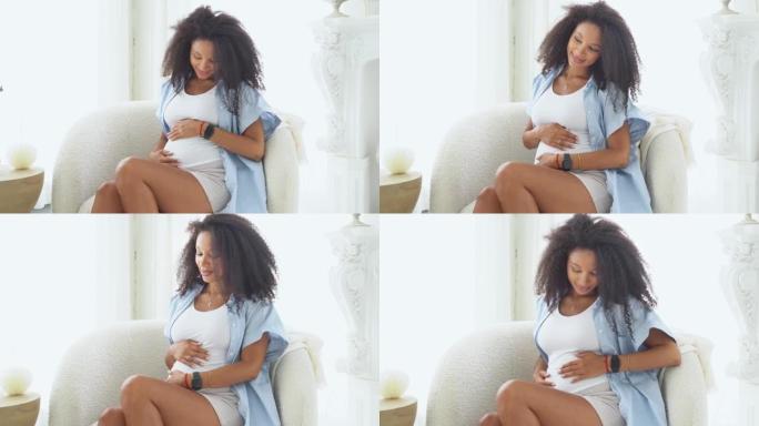 健康怀孕。黑色迷人的孕妇在白色卧室与大窗户坐在椅子上。美国黑人女性妊娠晚期，抚摸腹部。妈妈在等宝贝。