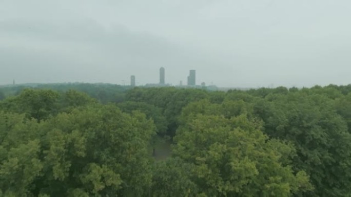 Drone rising over lush green trees with a city in 