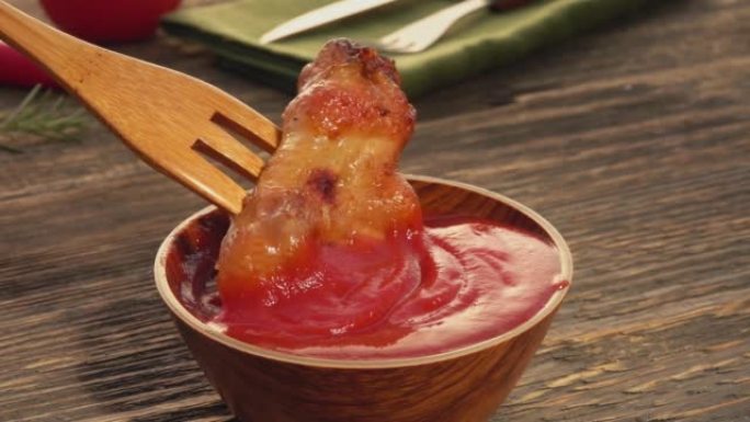 木叉的特写镜头将烤鸡翅浸入番茄酱中