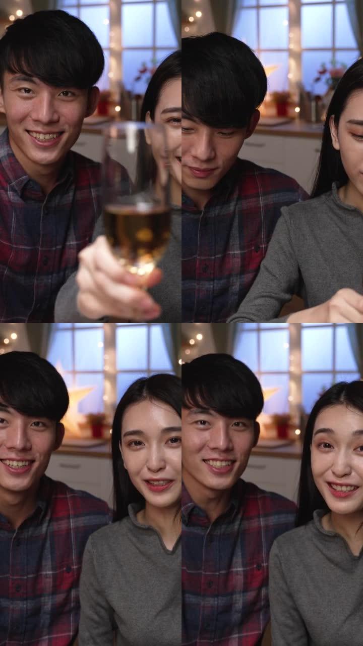 垂直屏幕: 两个女人和男人看着相机，拿着白酒杯和烤面包。夫妇在家庭厨房的圣诞节和新年视频通话中叮当作
