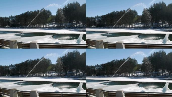喷泉里的水掉进了结冰的湖里。冬日晴朗，常青树和远处的人