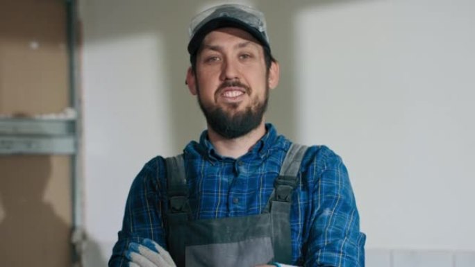 一名在建筑工地工作的男子穿着工作服棒球帽，双臂交叉在胸前看着镜头