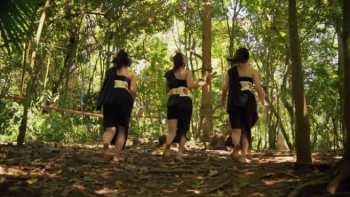 美丽的巴厘岛女子戴着金色的皇冠和黑色的衣服在森林附近一起快乐地奔跑
