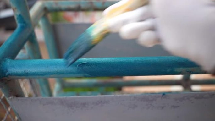 人用画笔画蓝色铁框，外部修复过程。除锈后在金属管上涂彩色涂料，阳台围栏重建