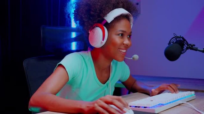 年轻的非洲裔美国妇女戴着耳机玩视频游戏和在线直播与麦克风在家里，游戏和esport或演员游戏，一个人
