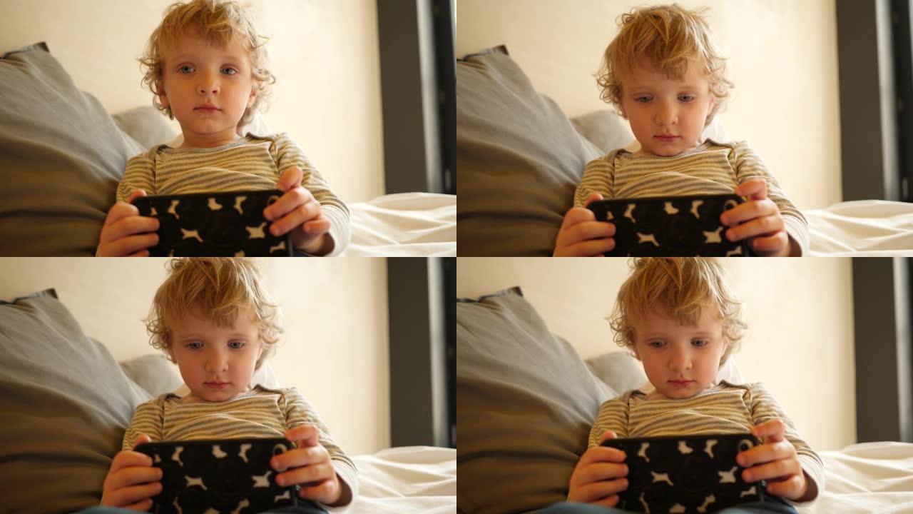 可爱的小男孩坐在床上看智能手机卡通