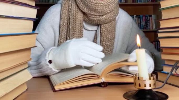 能源危机概念。缺乏暖气和电力照明。在图书馆使用蜡烛和保暖衣服阅读书籍裁剪人的视图。