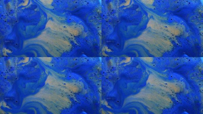 彩色的金粉和丙烯酸涂料散布在蓝色水彩表面上，以奇妙的设计和图案混合在一起。闪闪发光的金色颗粒、墨滴和