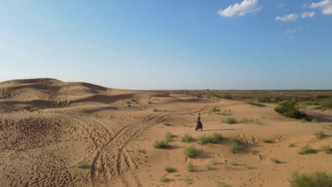 无人机的鸟瞰图。夏天，在阿斯特拉罕 (Astrakhan)，穿着长豹子连衣裙的女人沿着沙漠中的高沙丘