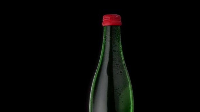 绿色一瓶红色瓶盖的矿泉水。水滴中的玻璃瓶在黑色背景上旋转